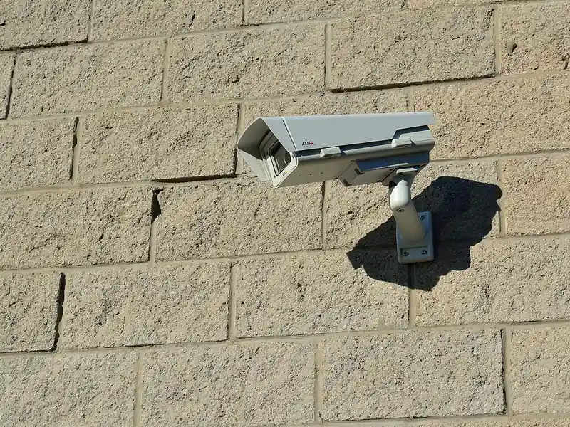 Generic white security camera mounted on a brick wall (illustrative photo)